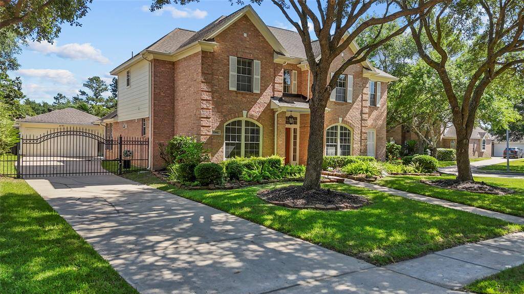Charming two-story brick home with a spacious driveway and gated entry. Surrounded by lush greenery and mature trees, it offers a welcoming curb appeal in a serene neighborhood setting.