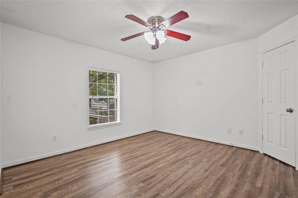 This room features a clean and bright space with white walls, a ceiling fan, and wood-style flooring. Natural light enters through a window, offering a welcoming atmosphere.