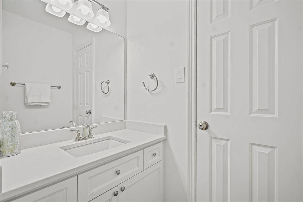 This is a bright, modern bathroom featuring a sleek white vanity with ample storage, a large mirror, and elegant lighting. The room is accented with chrome fixtures and a towel rack for convenience.