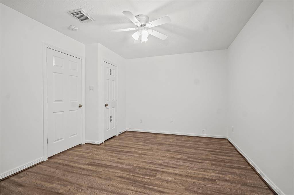 This room features clean white walls and a ceiling fan, with wood-style flooring for a modern touch. Two doors offer access to storage or additional spaces. Ideal for a bedroom or office.