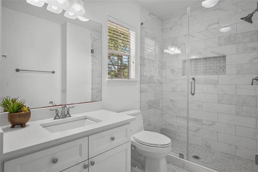Modern bathroom featuring a sleek white vanity, glass-enclosed shower with marble tile, and bright natural lighting.
