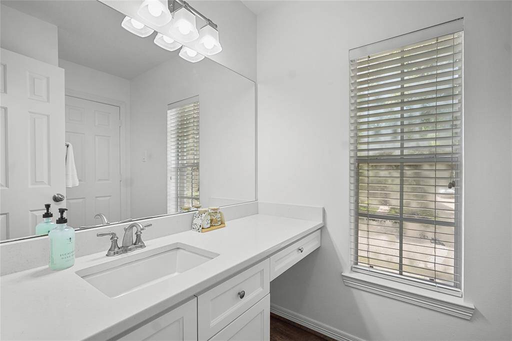 This bathroom features a clean, modern design with a white vanity, sleek fixtures, and a large mirror. Natural light streams through the window with blinds, enhancing the bright and airy feel.