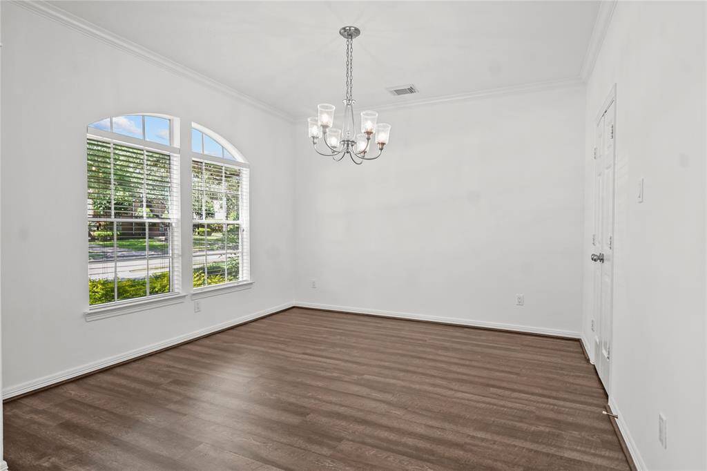 Bright dining room with a large arched window, hardwood floors, and a central chandelier. Ideal for gatherings.