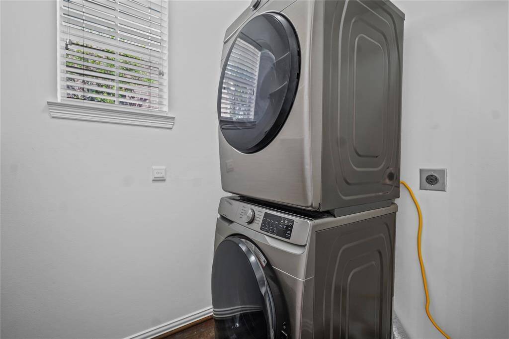 This photo shows a compact laundry room with a modern stacked washer and dryer set, next to a window that lets in natural light.