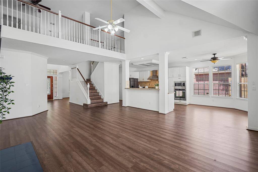 This spacious home features an open floor plan with high ceilings, a modern kitchen with stainless steel appliances, and abundant natural light. The hardwood floors and elegant staircase add a touch of sophistication, while the upper-level railing offers a stylish overlook of the living area.