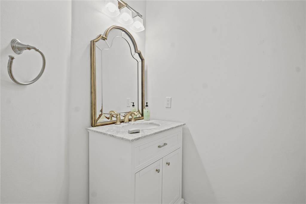 This bathroom features a chic vanity with a marble countertop, a stylish gold-framed mirror, and modern lighting. The minimalist design offers a clean and elegant look.