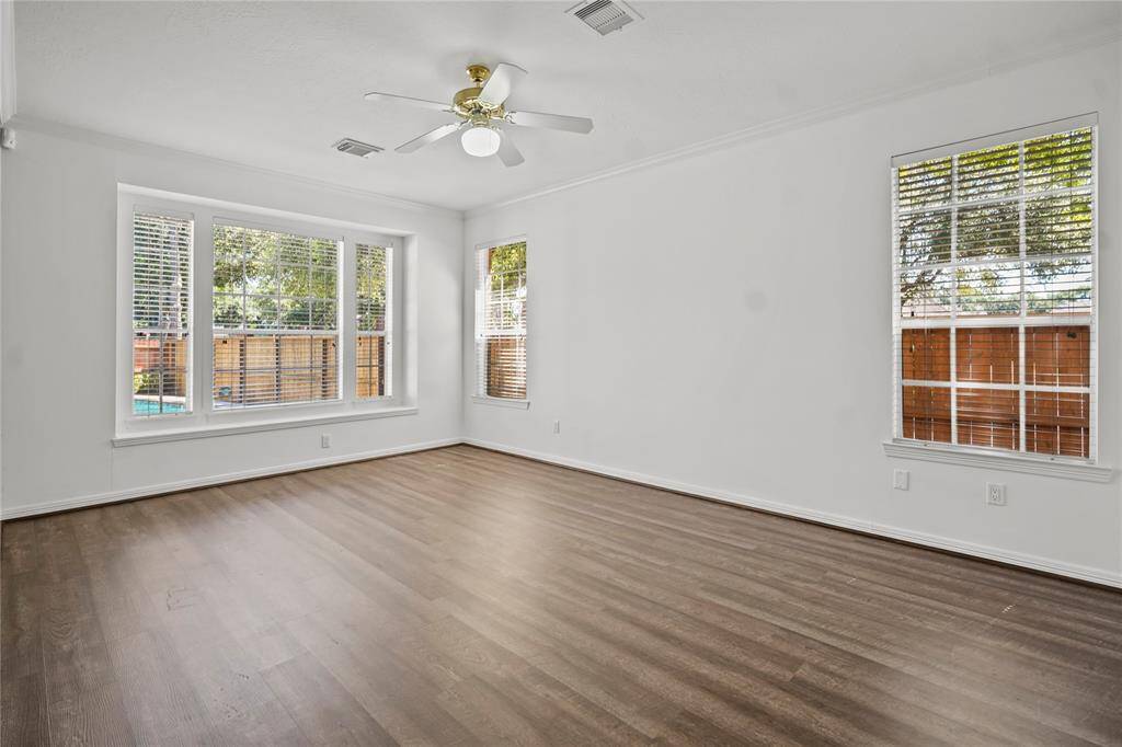 This spacious living room features large windows for ample natural light, neutral walls, wood flooring, and a ceiling fan, creating a bright and welcoming atmosphere.