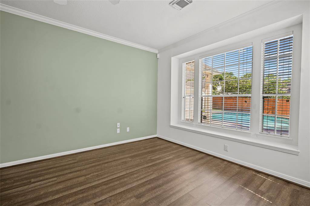 This room features a fresh green accent wall, hardwood flooring, and a large window with blinds overlooking a pool area, providing ample natural light.