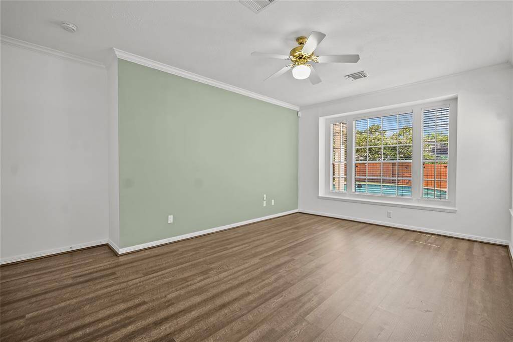 Bright, spacious room with a large window offering views of a pool. Features a light green accent wall, wood flooring, and a ceiling fan, combining modern style with comfort.