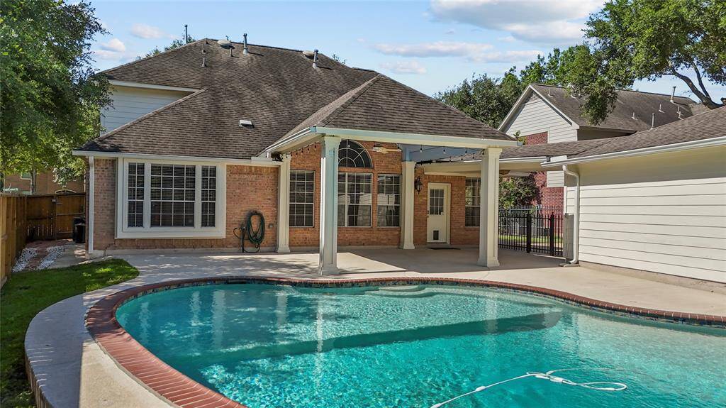 This home features a charming backyard with a covered patio and a refreshing in-ground pool, surrounded by a spacious, well-maintained deck. The brick exterior and large windows add to its inviting appeal, perfect for relaxation and entertaining.
