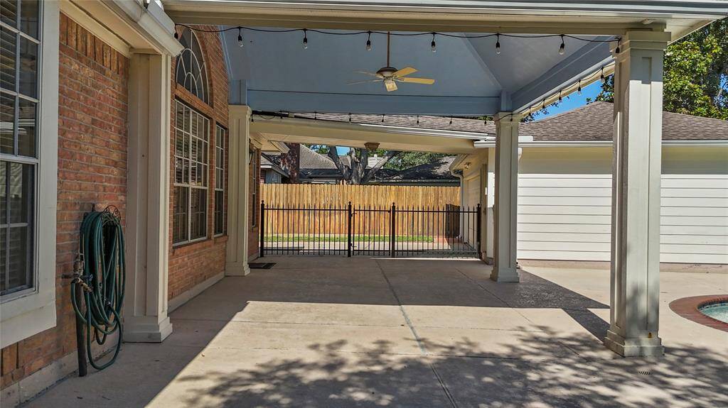 This photo showcases a spacious covered patio area with a ceiling fan, string lights, and a view of a fenced backyard. It features brick and siding exteriors, offering a versatile outdoor living space.