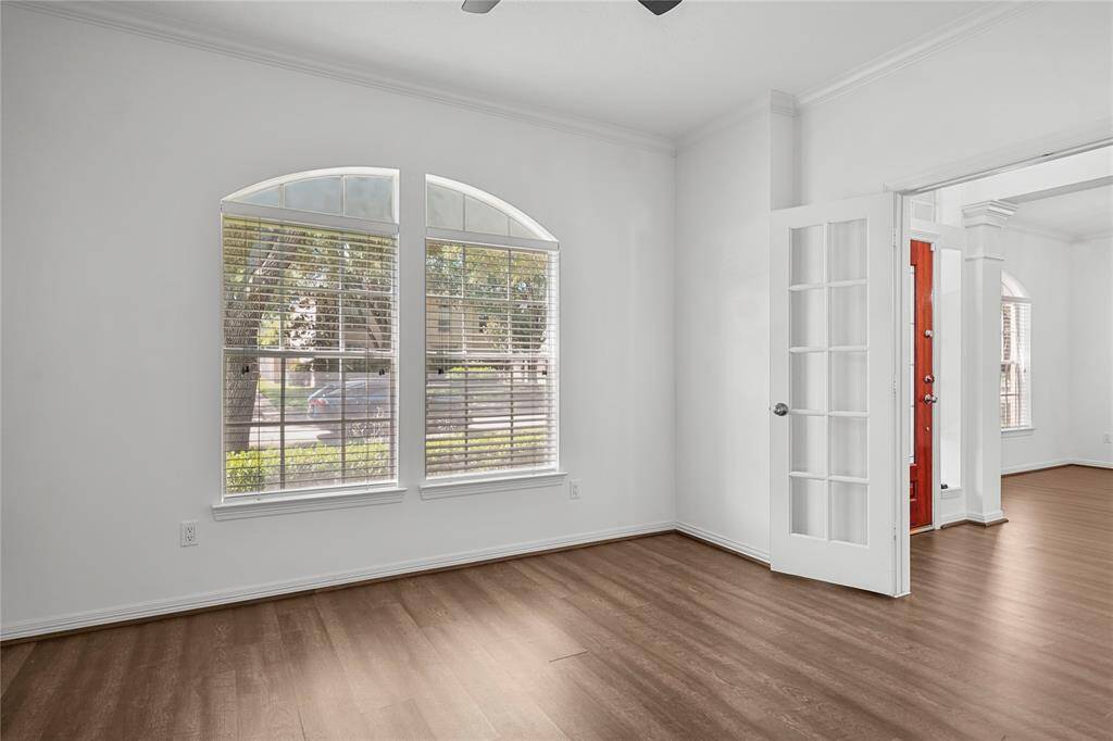 Bright room with large arched windows, wood flooring, and a French door leading to another space. Freshly painted walls and ceiling fan add to its charm.