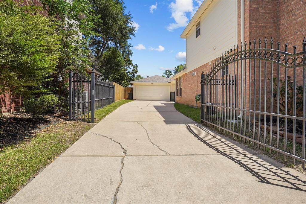 This photo shows a long driveway leading to a detached garage, framed by a wrought iron gate and fence. The pathway is lined with a mix of greenery and brick walls, offering a private and secure entrance.