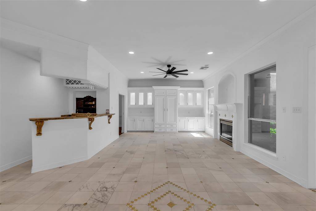 Well-lit living room features a modern ceiling fan, elegant fireplace, and large windows overlooking greenery. The open layout leads into a connected dining area, perfect for entertaining.