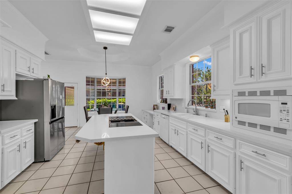 This bright kitchen features white cabinetry and countertops, a central island, and stainless steel appliances. It has ample natural light from large windows and a cozy dining area, creating a welcoming space for cooking and gatherings.