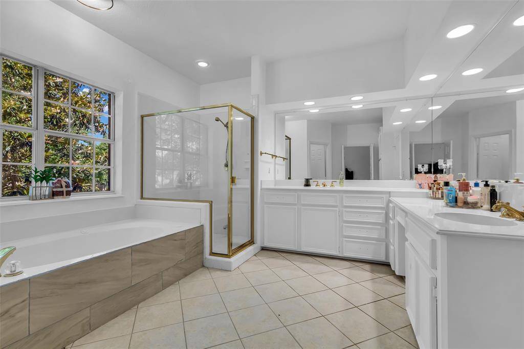 Spacious and bright bathroom featuring a large soaking tub, glass-enclosed shower, and dual sinks with ample counter space. Natural light streams in through a large window, enhancing the clean, modern design.