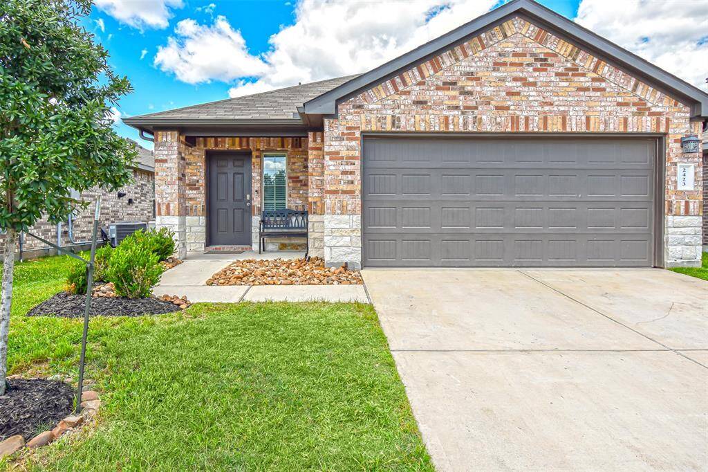 This is a modern, single-story brick home with a two-car garage and a neatly maintained front yard. The driveway is spacious, and the exterior features a mix of brick and stone accents.