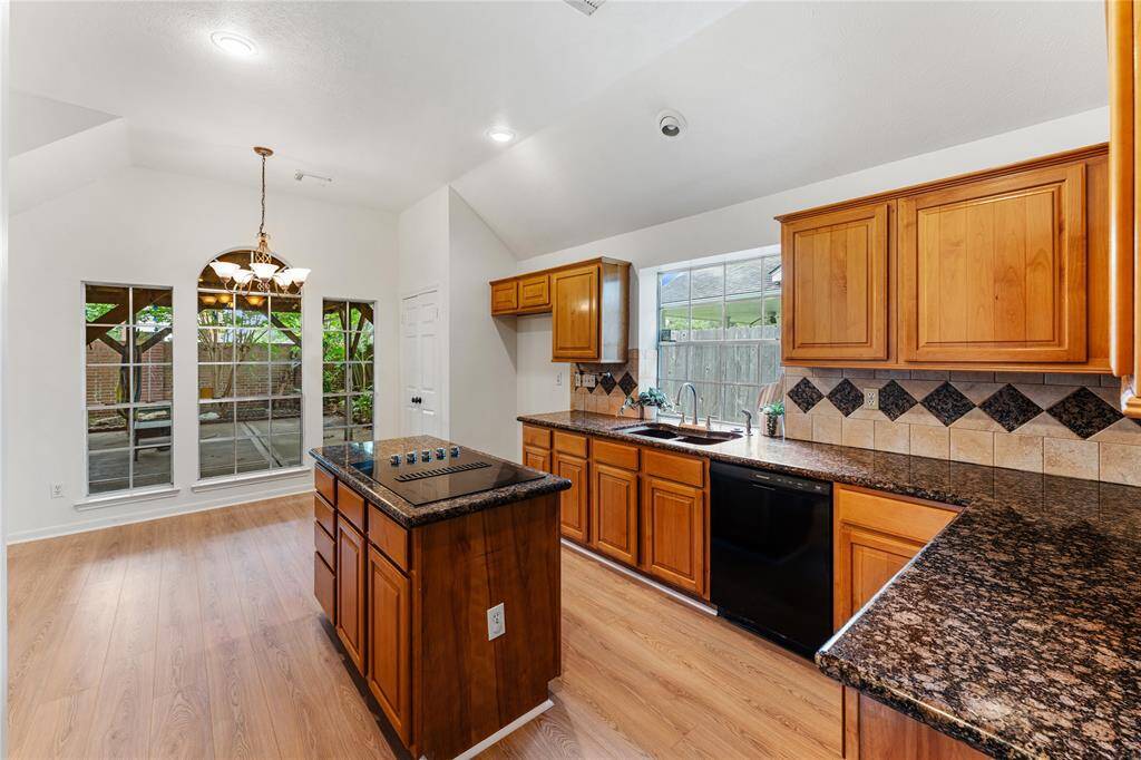 In the kitchen are granite countertops, and island cooktop, and undermount sink with bright window light.