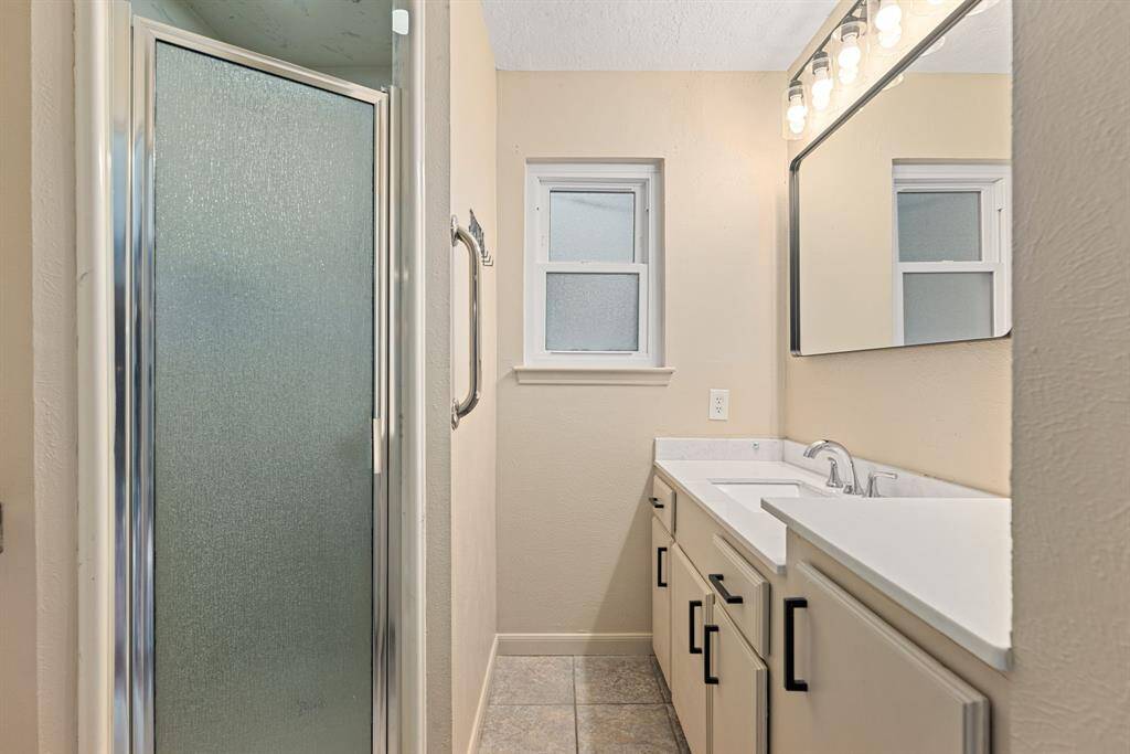 Primary bathroom features a frosted glass shower, large mirror with vanity lighting, and a spacious countertop with ample cabinet storage.