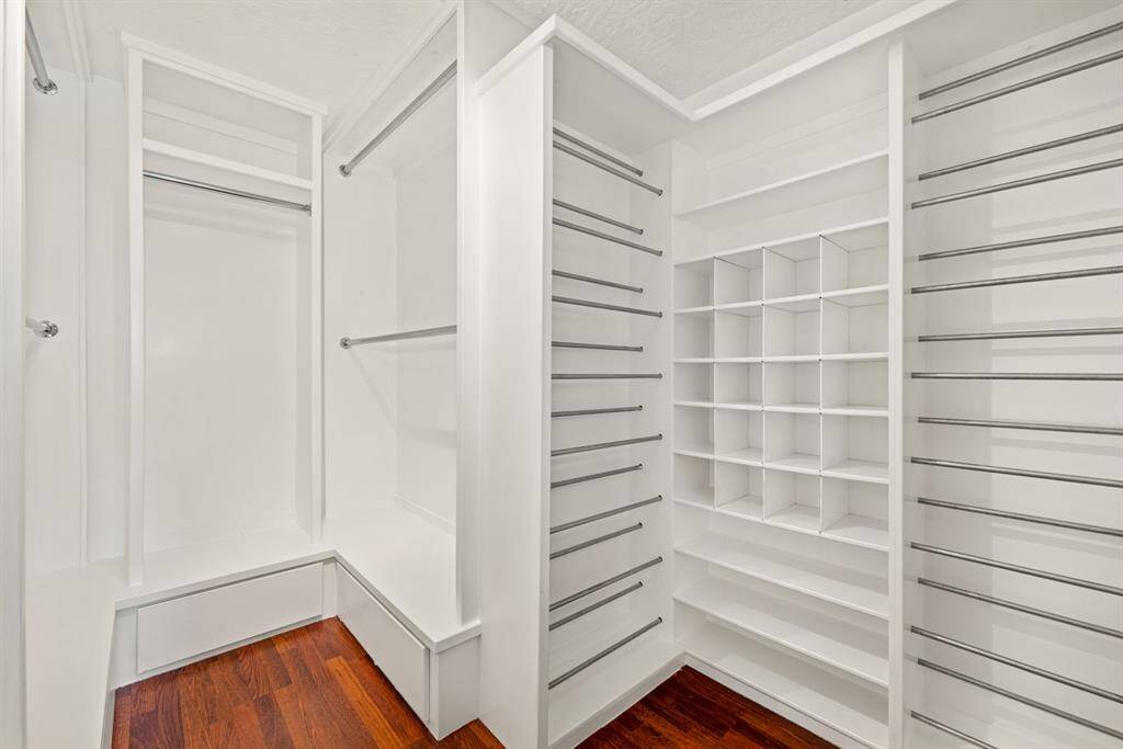 This photo features a spacious customized walk-in closet with white shelving, ample hanging rods, and built-in cubbies for organized storage.