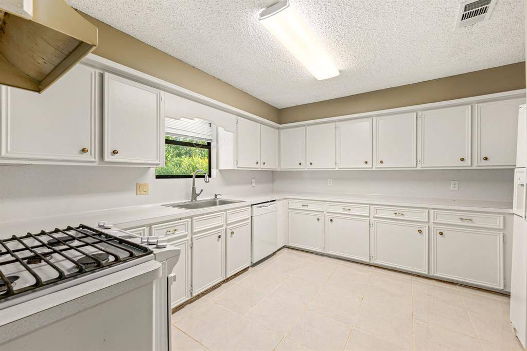 Bright kitchen with ample white cabinetry, a gas stove, refrigerator and tile flooring.
