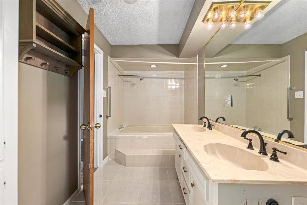 A tiled bathtub with double sinks in apartment.