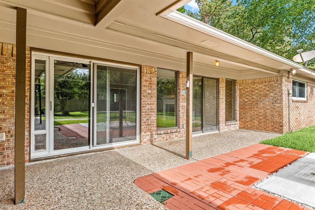 This photo showcases a covered patio area with sliding glass doors leading to a spacious backyard. The patio features a mix of brick and concrete flooring, providing a versatile outdoor space ideal for relaxing or entertaining.