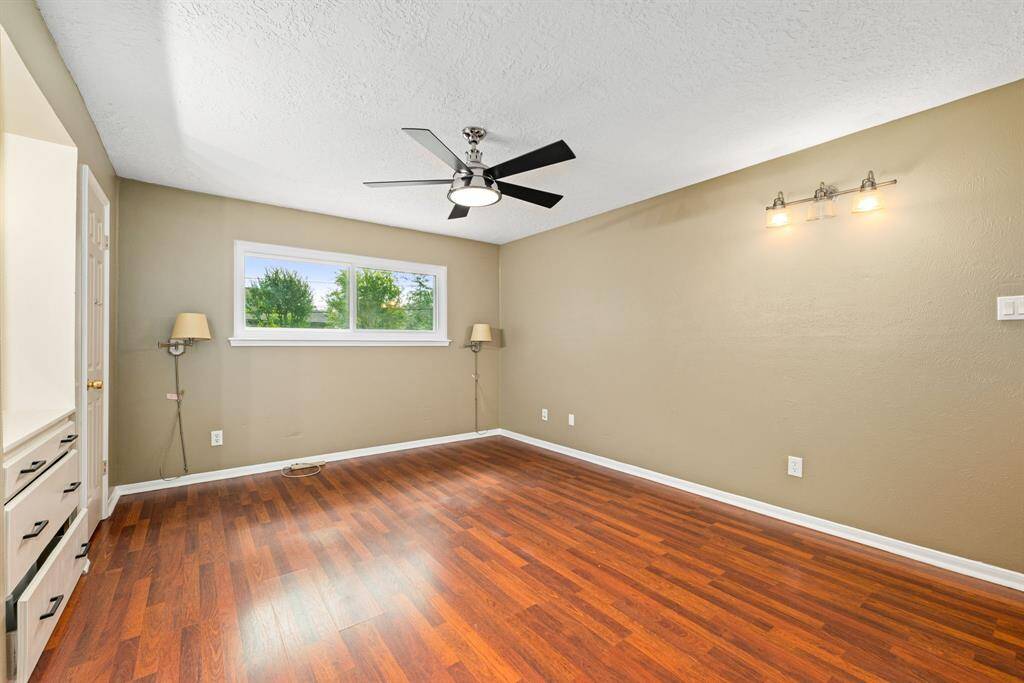 Bright, spacious primary room with hardwood floors, neutral walls, a ceiling fan and built in drawers.