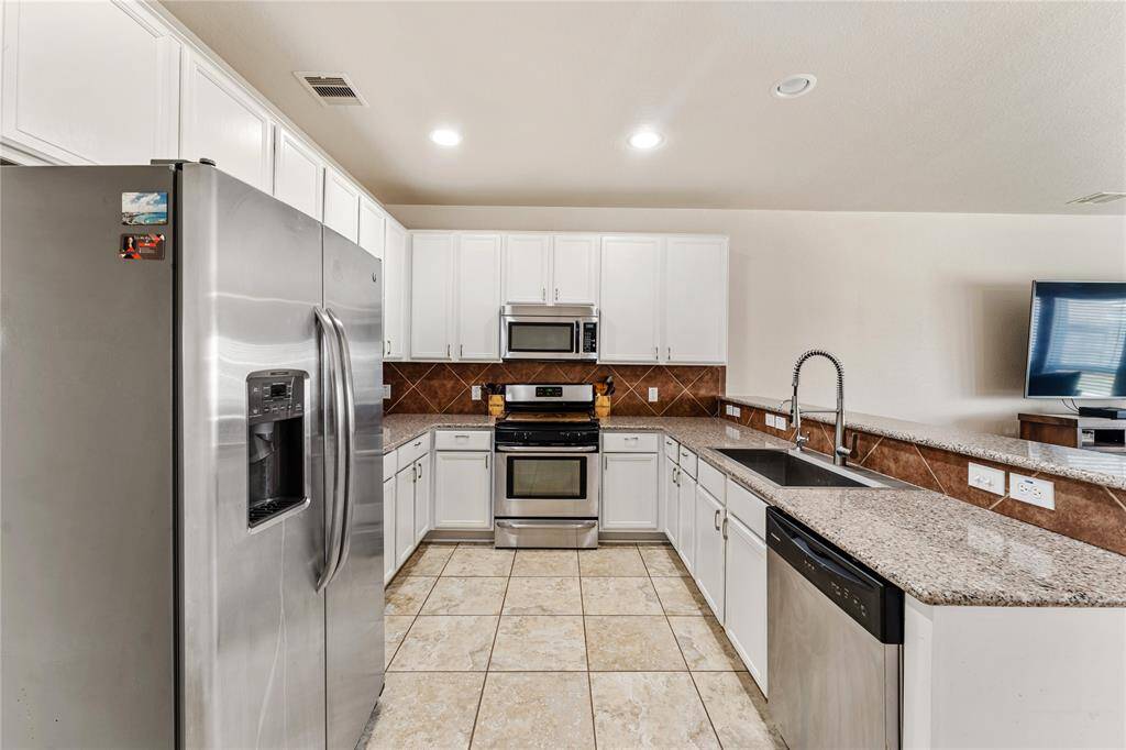 The Kitchen Features Modern Stainless Steel Appliances, White Cabinetry, Granite Countertops, And a Tile Backsplash. It Yields An Amazing View Of The Living Room and Back Yard