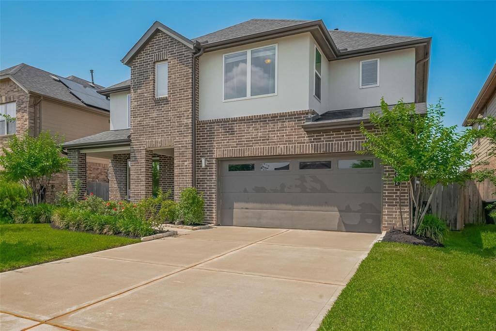This is a modern two-story home with a brick and stucco exterior, featuring a spacious driveway and a three-car tandem garage. The well-maintained front yard includes landscaped greenery, creating an inviting curb appeal.