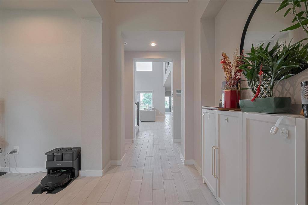 This photo showcases a bright, modern hallway with light wood flooring, leading to an open living space. The area is adorned with plants and has a clean, minimalist feel.