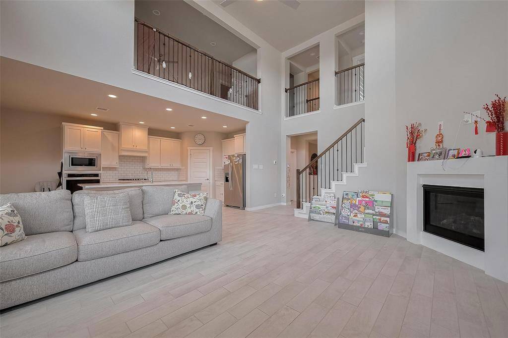 This spacious living area features high ceilings, an open floor plan, and abundant natural light. The modern kitchen includes white cabinetry and stainless steel appliances, while the cozy living space offers a fireplace and elegant staircase. Perfect for comfortable family living and entertaining.