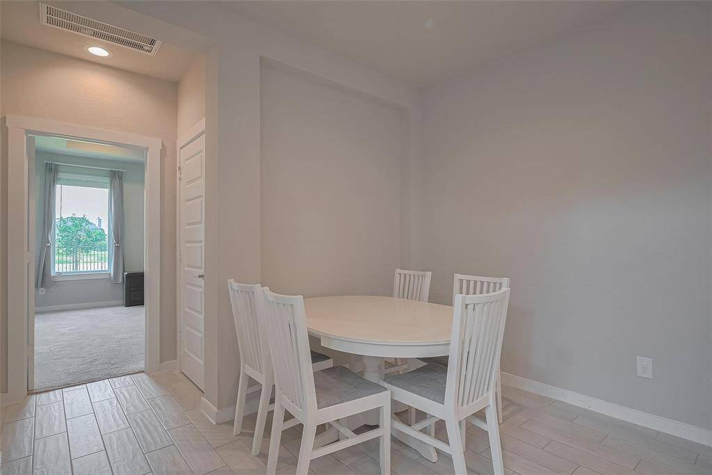 This photo shows a cozy dining nook with a round table and four chairs, featuring light-colored walls and flooring. The space is adjacent to a room with a large window, offering views of greenery outside.