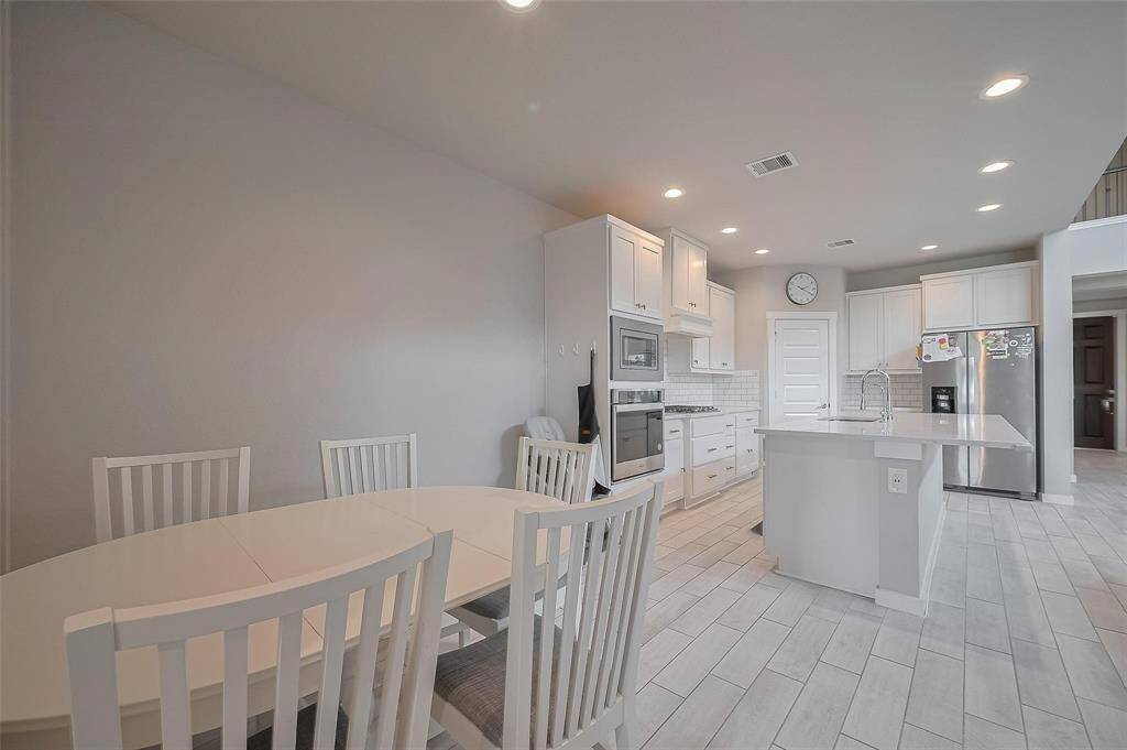 This photo showcases a modern, open-concept kitchen and dining area. The kitchen features sleek white cabinetry, stainless steel appliances, and a central island with a sink. The dining area includes a stylish table with matching chairs, all set on light-colored tiled flooring, creating a bright and inviting space.