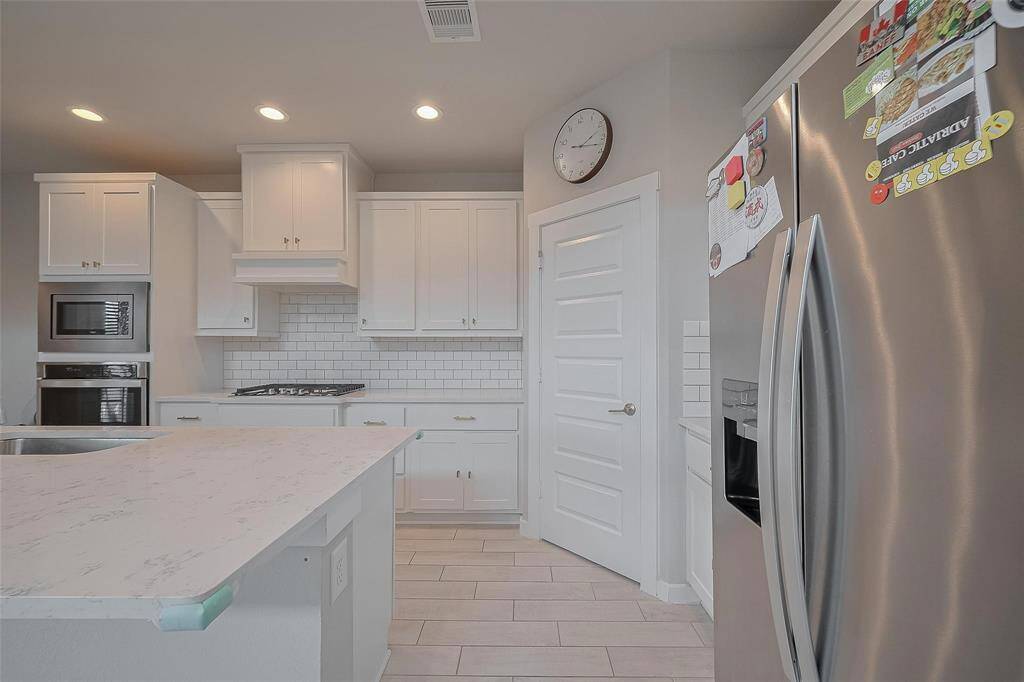 This kitchen features modern white cabinetry, stainless steel appliances, and a sleek tiled backsplash. The spacious layout includes a large island with a marble-style countertop, perfect for cooking and entertaining.