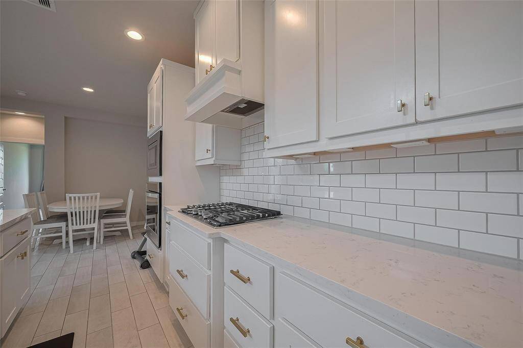 This modern kitchen features sleek white cabinetry, subway tile backsplash, and a built-in gas cooktop. The space is bright and airy, leading to a cozy dining area with a round table and chairs, perfect for family meals.
