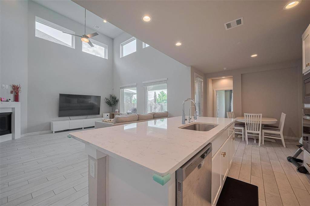 This spacious open-plan living area features high ceilings with abundant natural light, a modern kitchen with a large island, and a cozy seating area. Perfect for entertaining, it seamlessly connects to a dining space and offers a comfortable, airy environment.