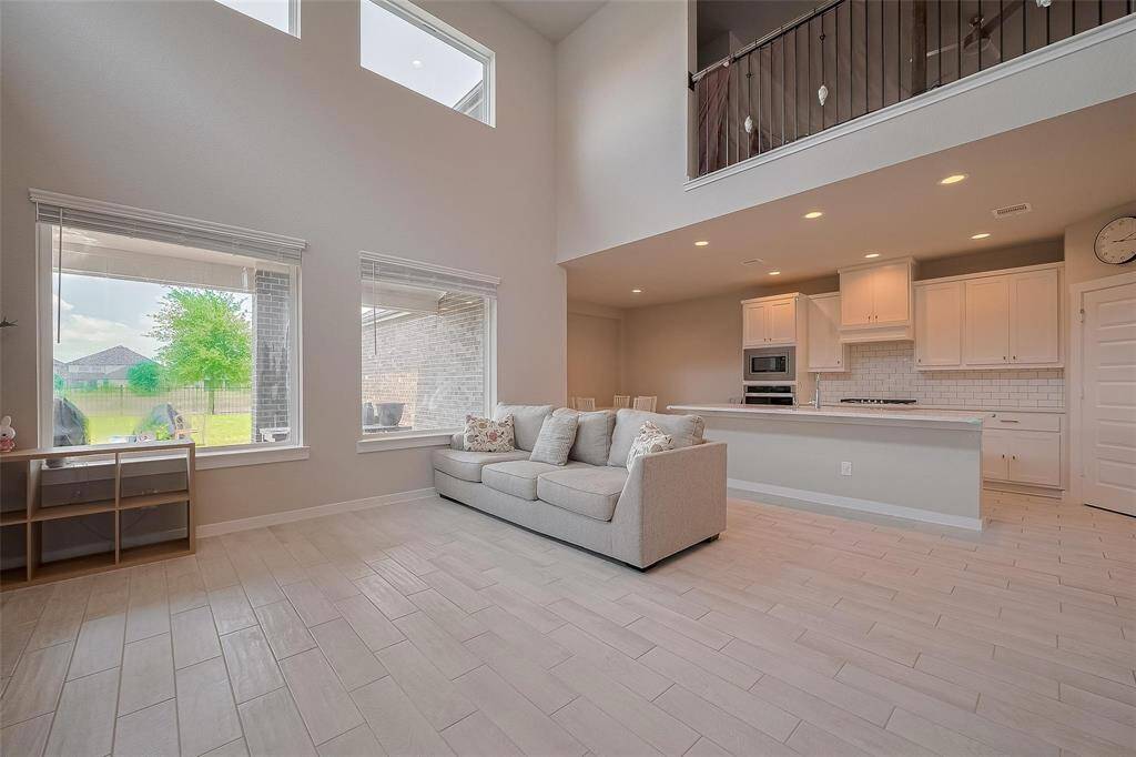 Bright and spacious open-concept living area with high ceilings and large windows. It features a modern kitchen with white cabinetry and a cozy seating area, overlooking a green backyard. Perfect for family living and entertaining.