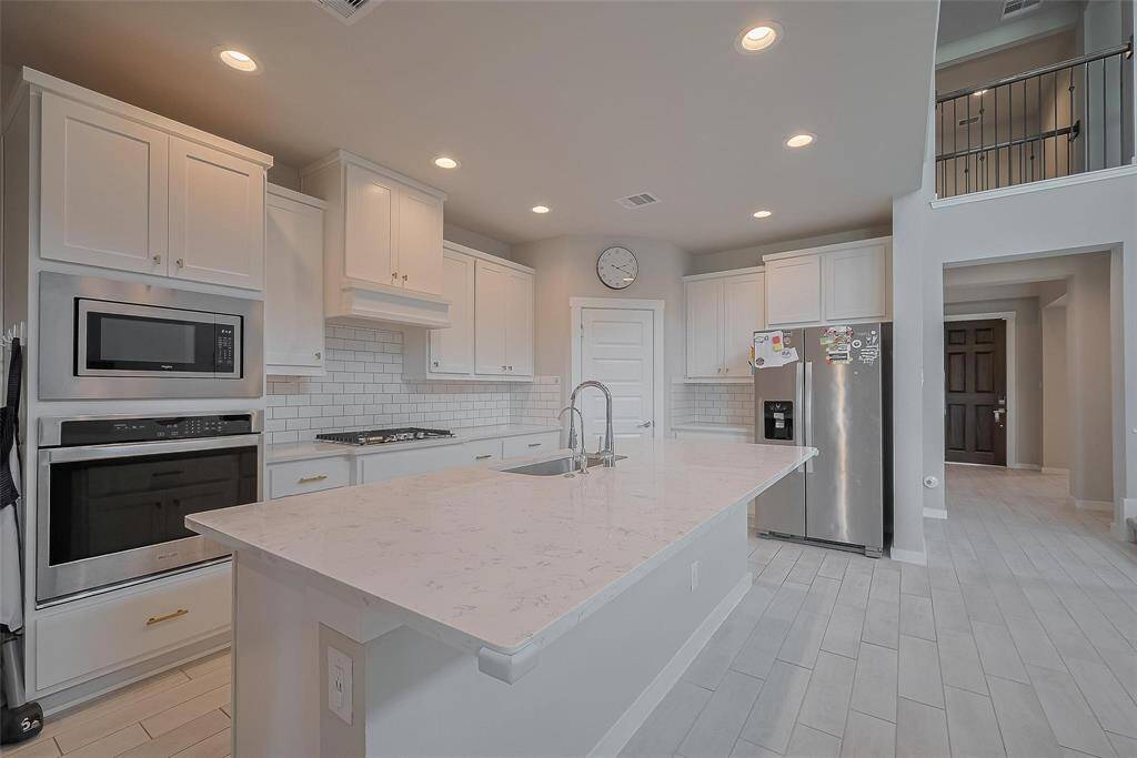 Modern kitchen with white cabinetry, stainless steel appliances, and a spacious island with a built-in sink. The open layout is complemented by recessed lighting and a stylish tile backsplash, creating a bright and inviting atmosphere.