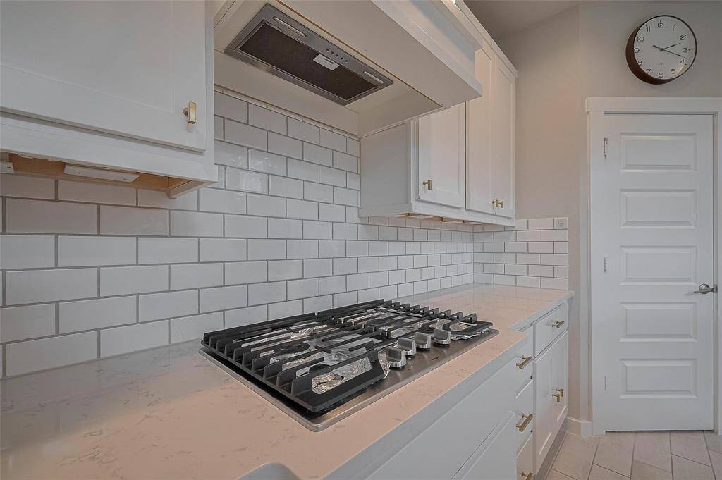 This modern kitchen features sleek white cabinetry, a stylish subway tile backsplash, and a gas stovetop set in a light quartz countertop, offering a clean and contemporary look.
