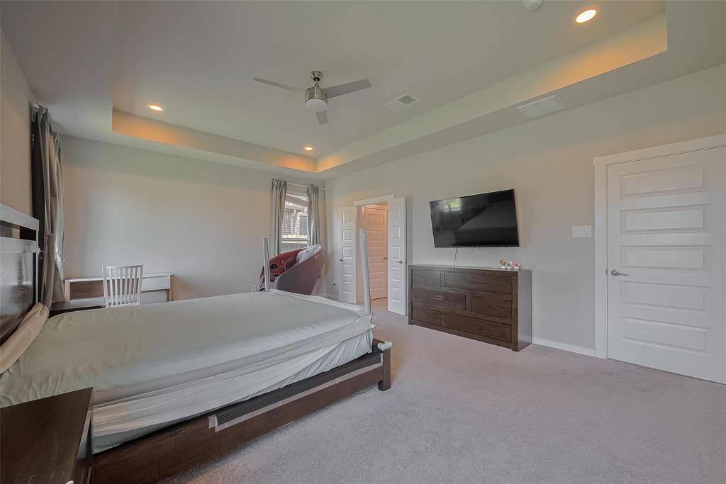 This spacious bedroom features a modern design with a recessed ceiling and ceiling fan.