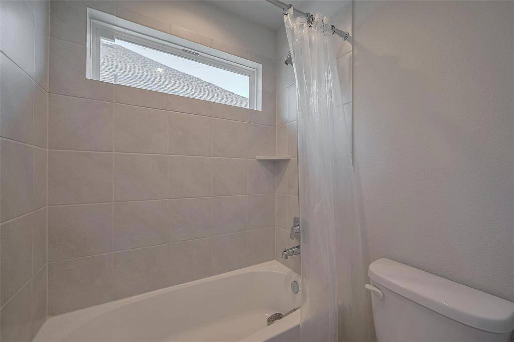 This bathroom features a modern tub and shower combo with light-colored tile, a small window for natural light, and a sleek white toilet.