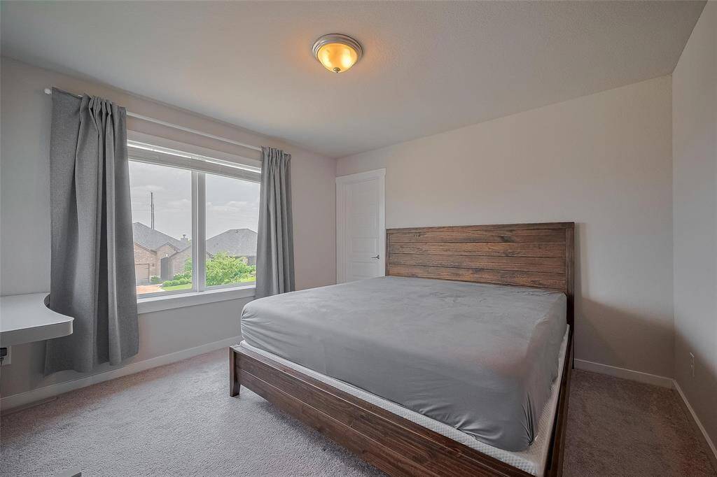 This bedroom features a large window with natural light, neutral walls, and carpeted flooring.