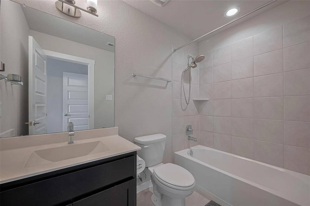 This bathroom features a modern design with a sleek vanity, a large mirror, and a tiled shower-tub combo. It's well-lit and offers a clean, neutral aesthetic.