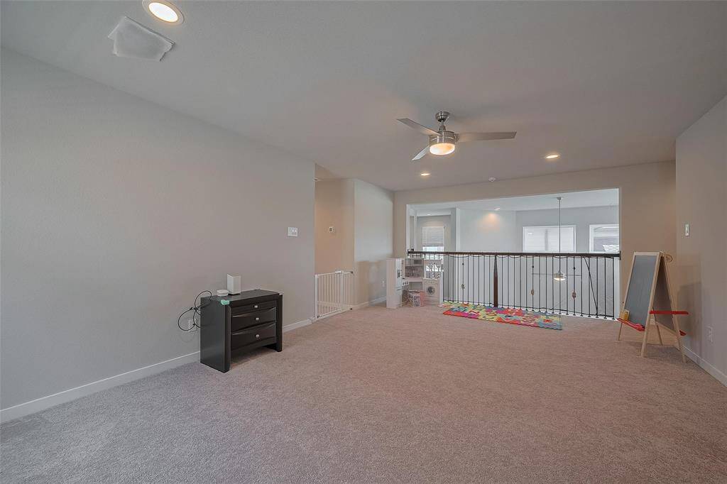 This photo showcases a spacious, light-filled loft area with neutral carpeting, recessed lighting, and a ceiling fan. It features a railing overlooking the floor below, making it an ideal space for a playroom.