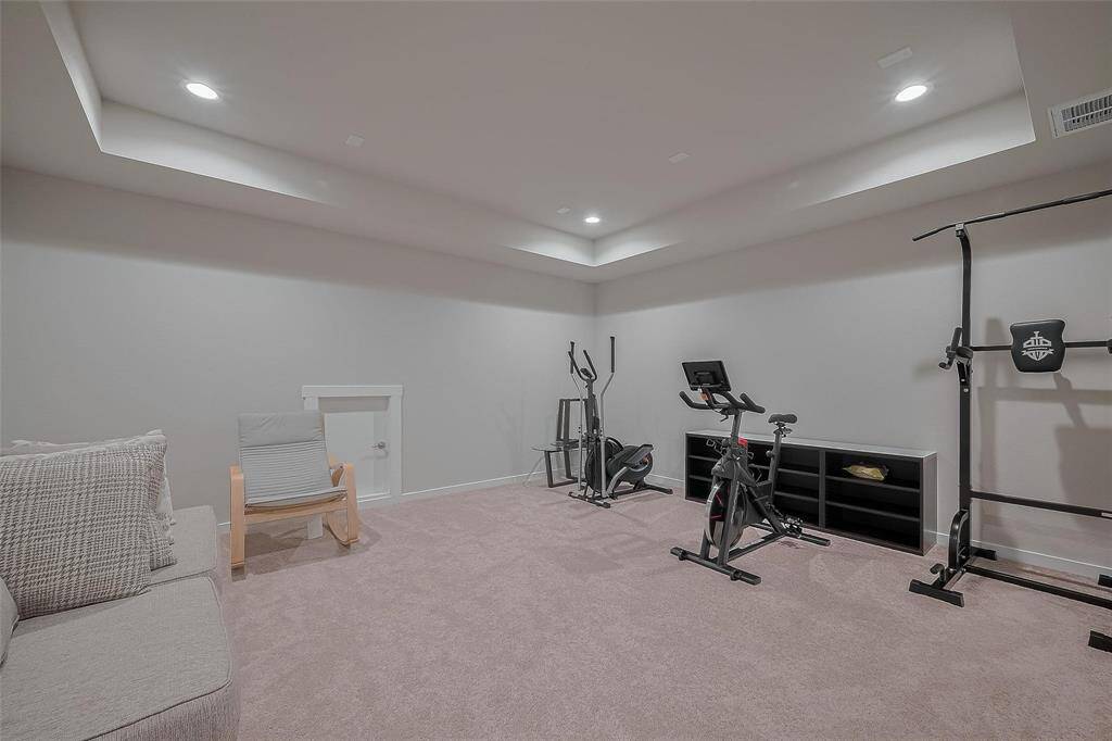 This spacious, carpeted room is ideal for a home gym or recreational area. It features recessed lighting, a cozy seating area, and ample space for exercise equipment. The neutral walls and ceiling create a bright, inviting atmosphere.