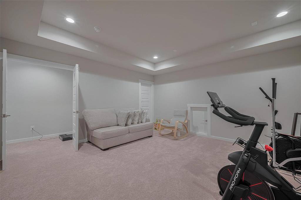 This spacious room features soft carpeting, recessed lighting, and a neutral color scheme. It includes a cozy sofa, a rocking chair, and an exercise bike, offering a versatile area for relaxation or workouts.