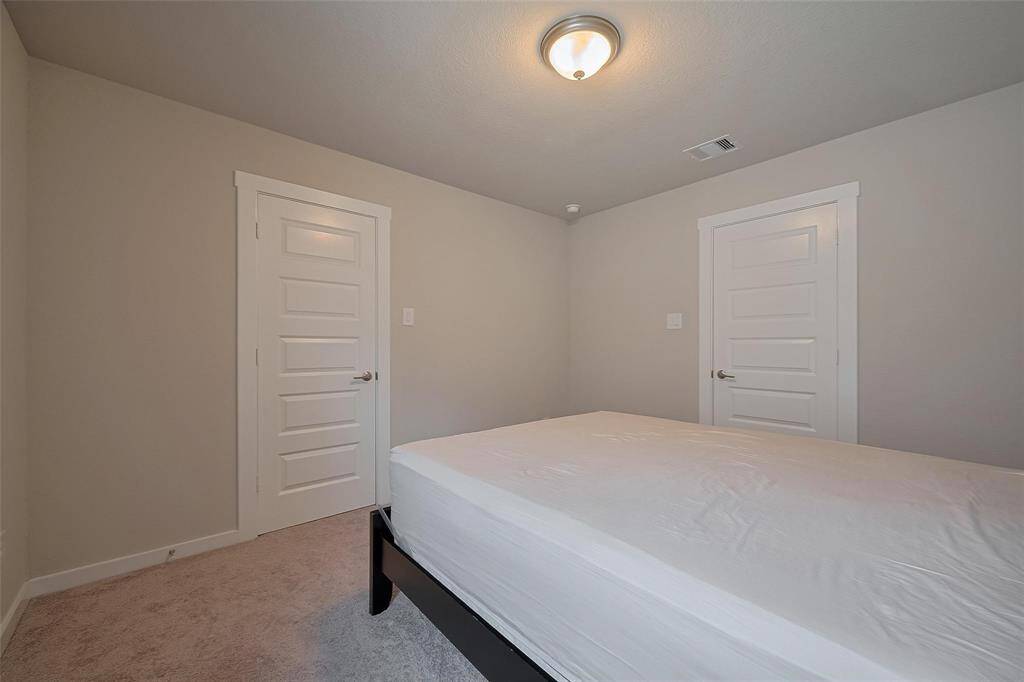 This is a clean, neutral-toned bedroom featuring a bed, carpeted floor, and two white paneled doors, offering a cozy and simple space.