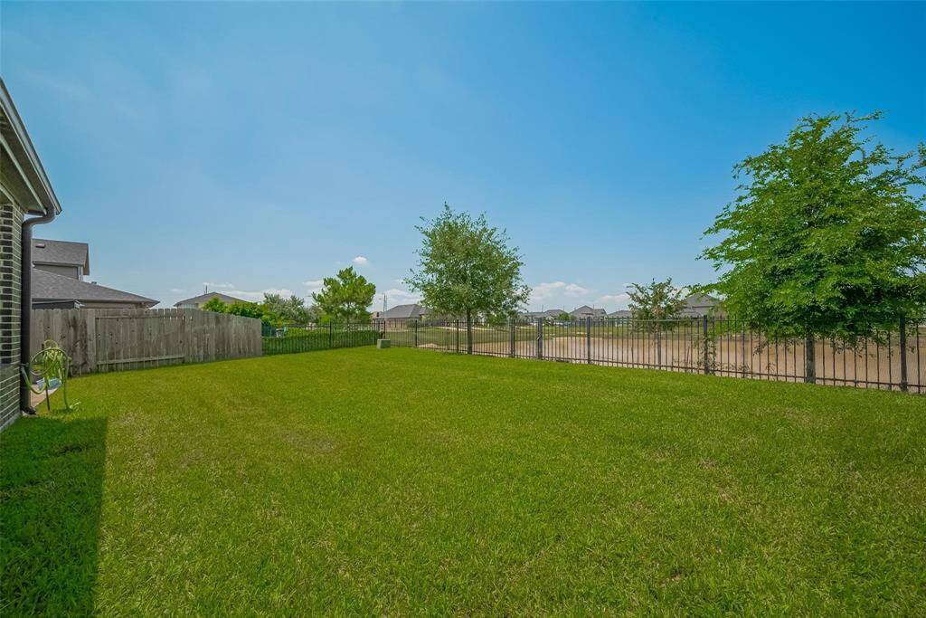Spacious backyard with a well-maintained lawn, bordered by a wooden and metal fence. It offers open views and features several trees, ideal for outdoor activities and relaxation.