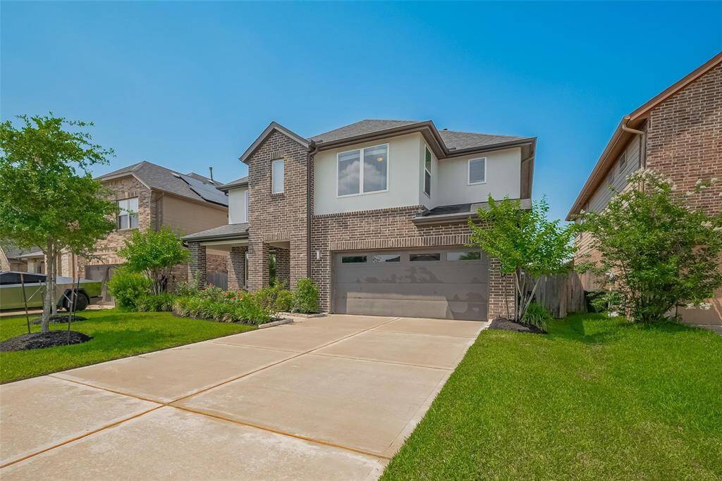 This is a modern two-story brick home with a well-maintained front yard, featuring a spacious driveway and a three-car tandem garage. It has a clean, inviting exterior with attractive landscaping.